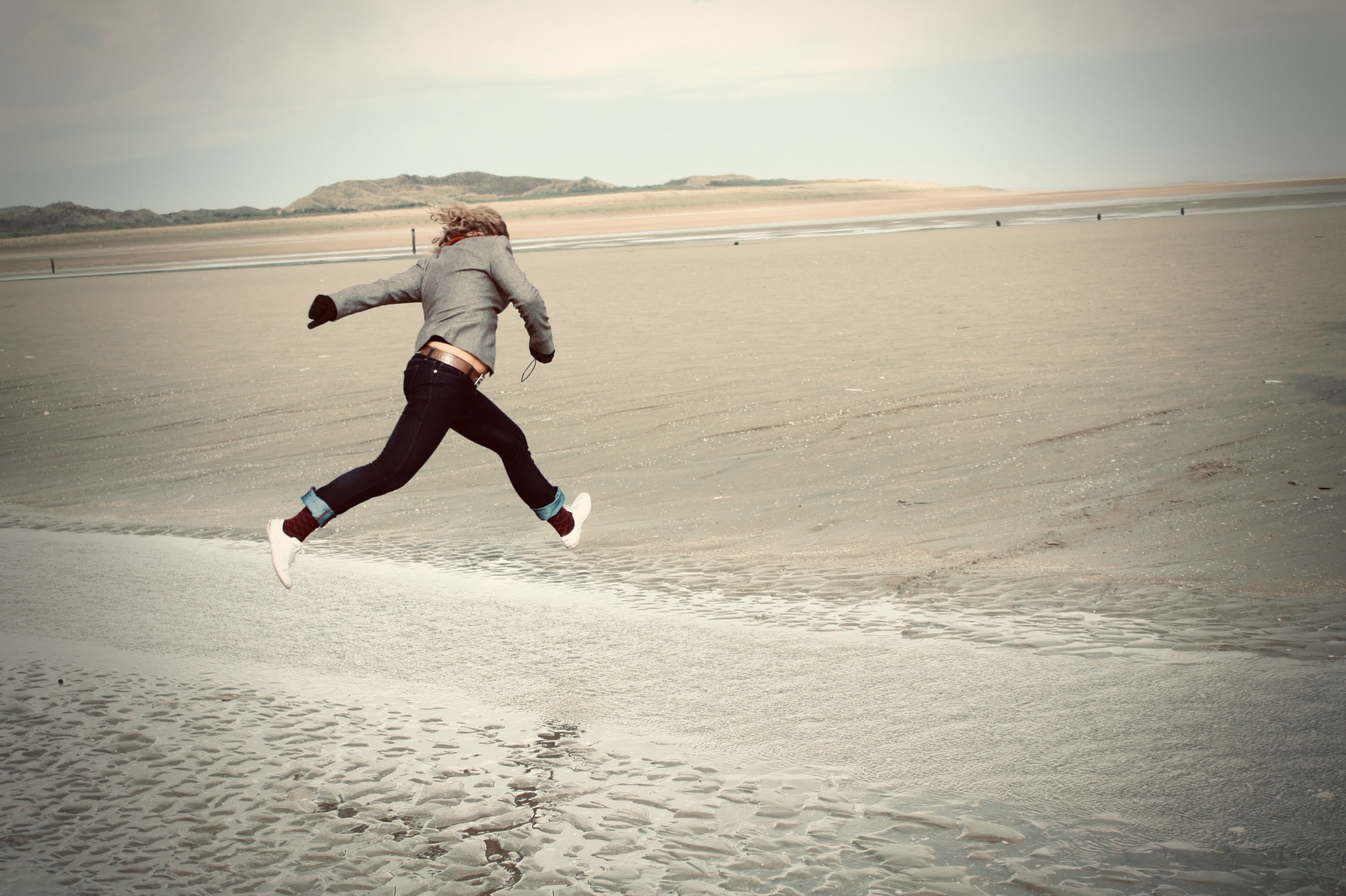 A figure mid-leap across a beach — captured in the air between footprints.